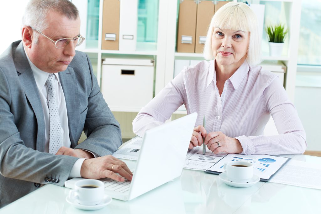 Kobieta i mężczyzna w eleganckich garniturach omawiający kwestie podatkowe i prawne, korzystając z komputera i dokumentów w biurze